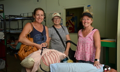 Three women holding pillows while smiling for the camera in front of bunk bends