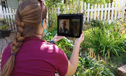Woman in a garden talking with an older man through a videocall on a tablet.