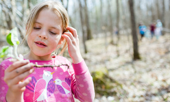 A girl in a wooded area looking at a feather.