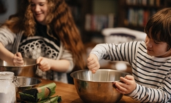 Two kids squeezing ingredients into a metal mixing bowl