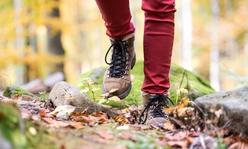 A close up of someone's feet wearing hiking boots while walking in fall foliage.