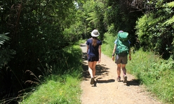 Two teens walking on a gravel path in a wooded area.