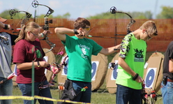 Youth aiming bows and arrows at a row of targets.