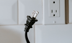 A black electrical cord being unplugged from a white wall outlet