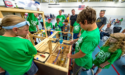 A group of youth wearing green 4-H shirts working on a wooden structure.