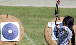 A girl aiming a bow and arrow at a target.