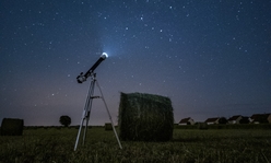 A night scene of a telescope set-up in a hay field.