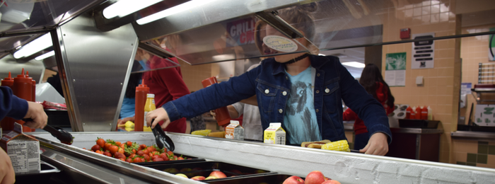 A student moving through a school cafeteria line of healthy food options.
