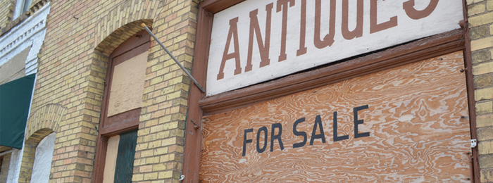 Antique shop with boarded up windows and a for sale sign