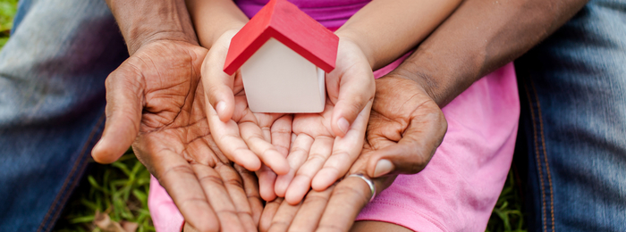 A parent and child's hands holding a small model of a house