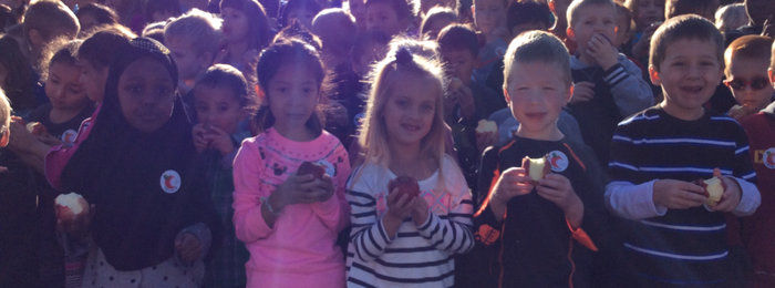 A group of elementary students outside with apples.