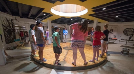 A group of youth standing in a circle with the light from a round skylight shining in the center of the circle.