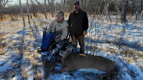 Man in track wheelchair with hunted deer on the ground