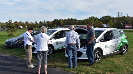 Adults looking and three different electric vehicles.