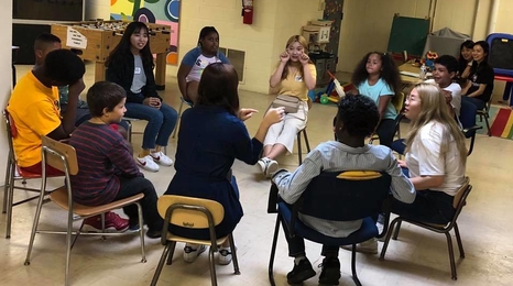 Group of tweens sitting in a circle on chairs in a classroom.