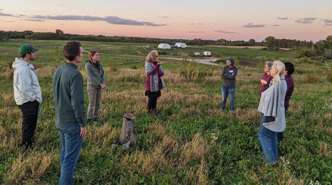 Group of adults standing in a field with a beautiful sunset in the background.