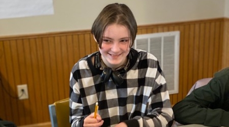 A youth member holding a pencil while sitting at a table with a workbook in front of them.