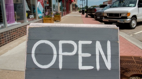An open sign outside of storefront on a Main Street in a small town.