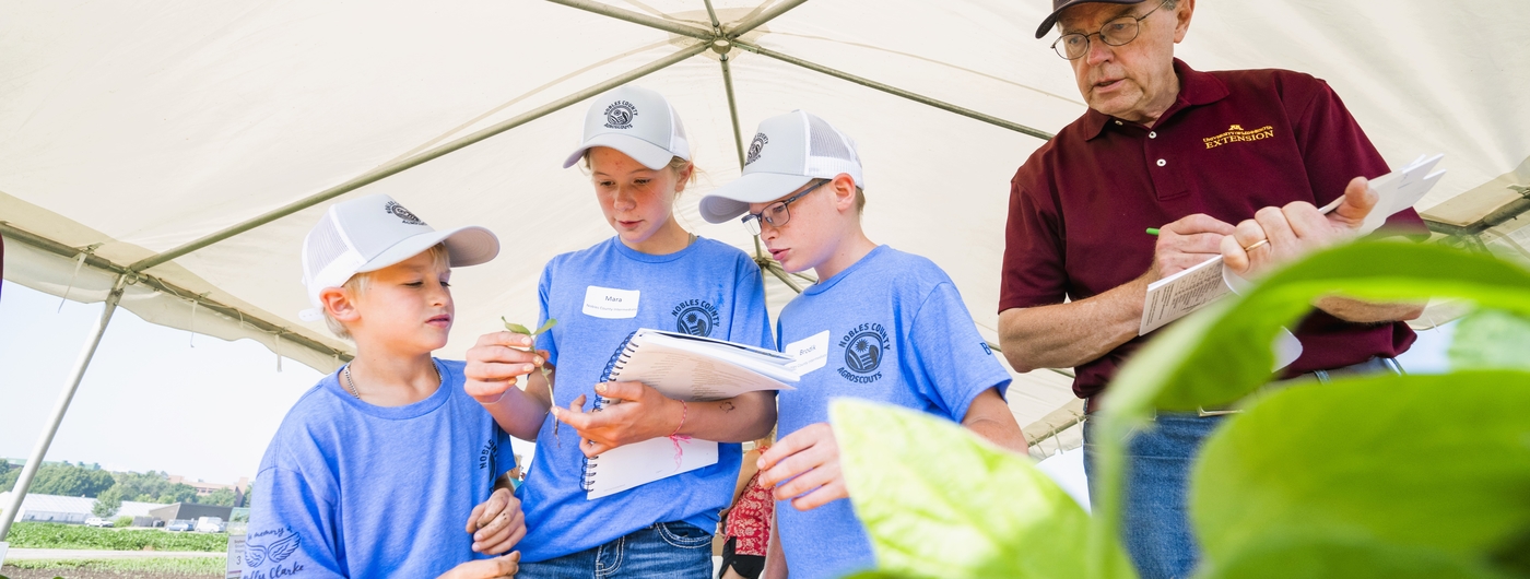 Three youth under a tent make a plant observation, guided by an adult educator