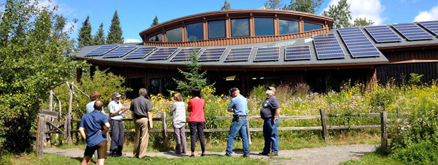 Group of adults standing in front of the Hartley Nature Center building looking at the solar panels on the roof.