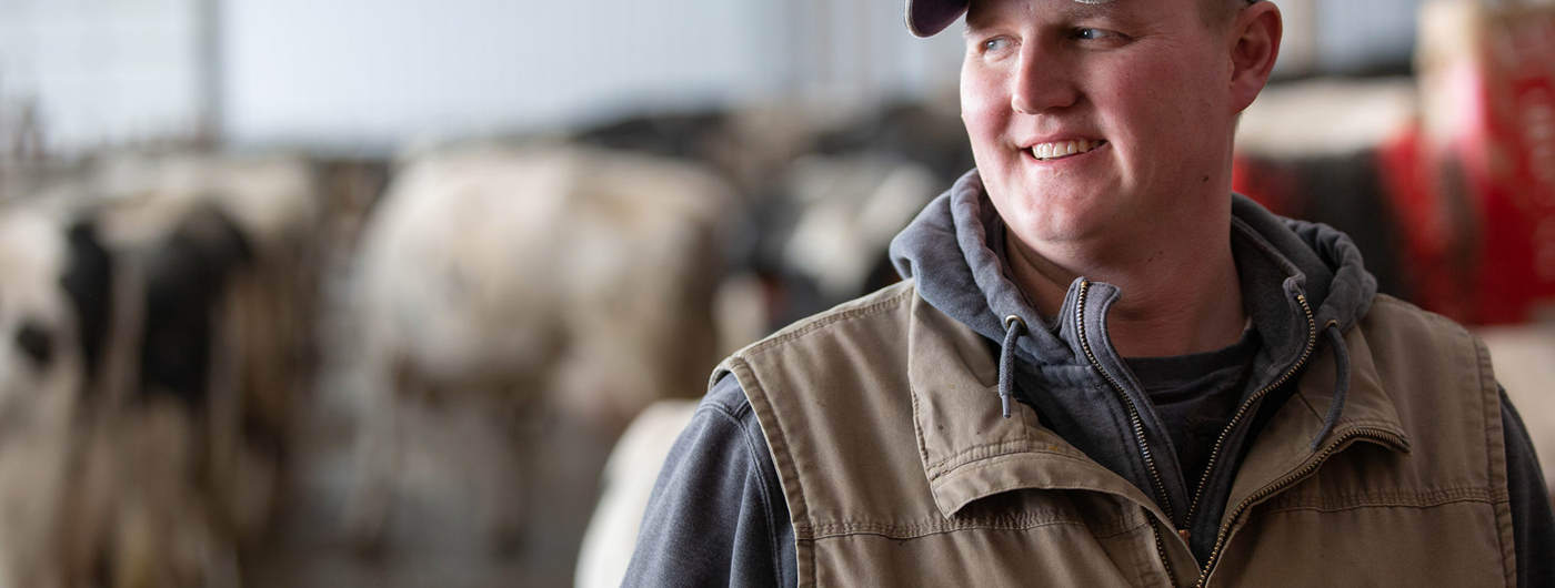 A male dairy farmer in a barn with cows in the background.