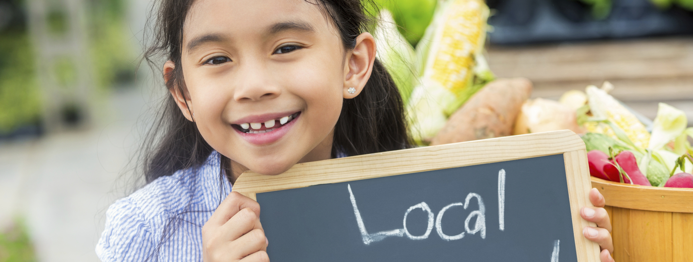 smiling girl holding chalkboard sign local produce