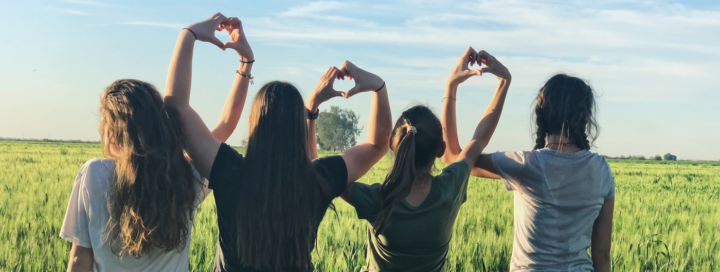 A line of girls in a open field making hearts with their hands.