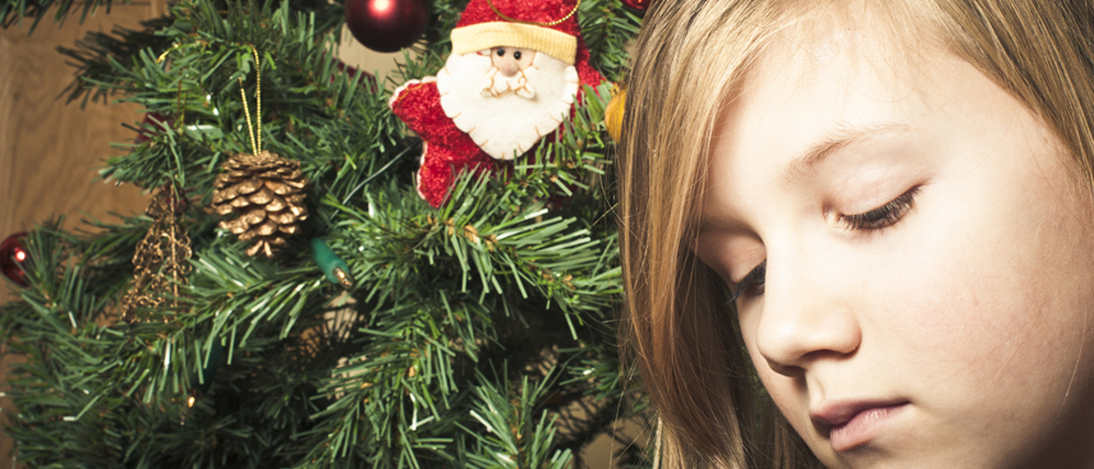 Child looking sad in front of Christmas tree