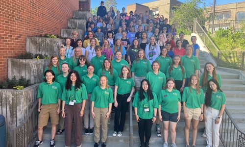 A group of youth standing on stairs with the first three rows of youth wearing 4-H green polos