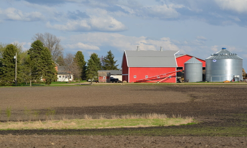 Farmstead in spring with just plowed field in foreground.