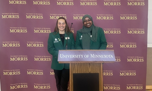 Minnesota 4-H State Ambassadors wearing official green blazers while standing behind a University of Minnesota podium.