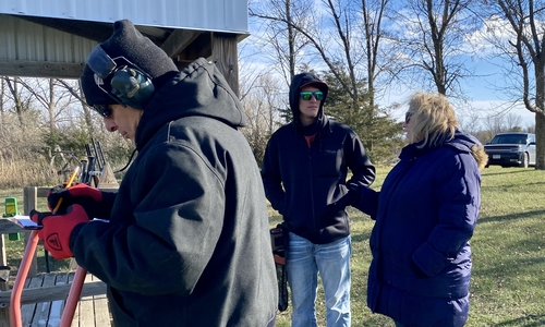 Two adult volunteers with a youth member at a 4-H outside at a fall trap league practice.