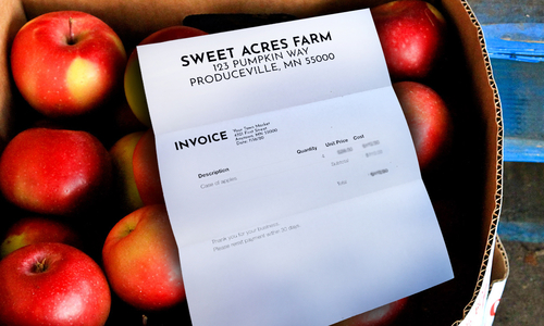 Box of apples with a paper invoice lying on top of the apples from "Sweet Acres Farm, 123 Pumpkin Way, Produceville, MN 55000."