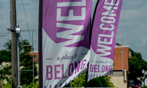 Welcome a place to belong text on two large signage flags near a Main Street road leading into a town.