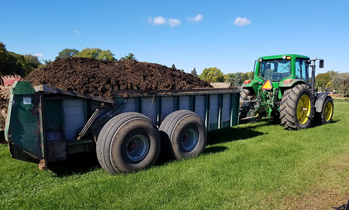Composted manure being hauled by a tractor on a field.