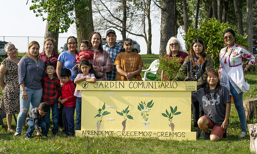 A group of gardeners pose behind the "Gardin Comunitario" sign.