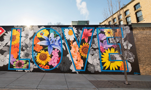 A mural of flowers with the word love in big letters on a building in Northfield, Minn by artist Brett Whitacre.