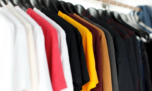 Shirts in a variety of colors hanging on a clothing rack. 