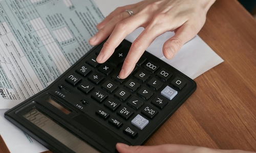 A woman's hands using a black calculator on top of tax forms on a desktop.