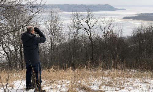 Person looking through binoculars at a river in winter.