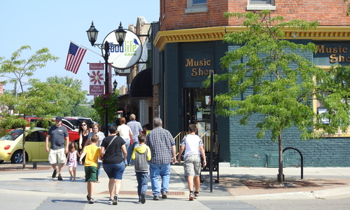 People walking down a small town street near a music store. 