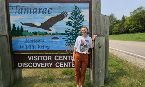 Myra McKee parada frente al cartel de bienvenida del Refugio de Vida Silvestre Tamarac