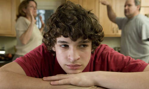 Teen boy resting his chin on his hands listening to parents fight.