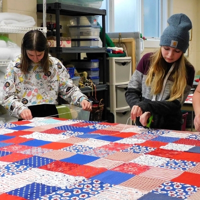 An adult and two teens make a red, white and blue quilt