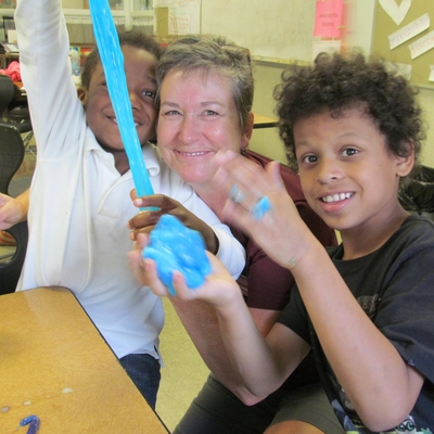 Two boys stretching blue slime while an adult woman smiles by them.