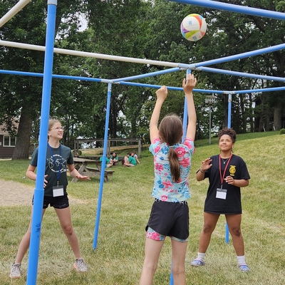 Three girls playing a game with a volleyball outside.