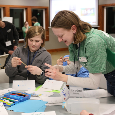 A 4-H state ambassador wearing an official green shirt helping youth members create desk name plates.