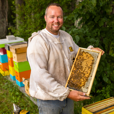 Man standing in apiary holding a frame from a beehive.