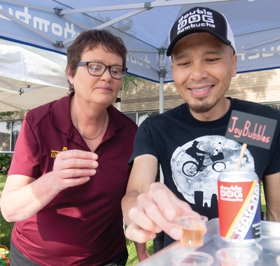 Suzanne Driessen helps Lee Vang offer kombucha samples safely
