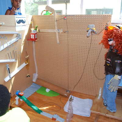A young person looks at a Rube Goldberg Machine that has tracks and a mannequin.